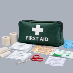Green compact first aid kit with white cross and first aid text, surrounded by bandages, dressings, plasters, wipes and gloves.