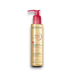 Bioderma Sensibio Micellar Cleansing Oil in a 150ml (5 FL.OZ.) transparent gold-colored bottle with a red pump dispenser. The label features the 'Bioderma' logo at the top, with the product name 'Sensibio Micellar Cleansing Oil' written in black and pink. The description highlights its soothing makeup-removing properties, including its ability to remove impurities and waterproof makeup. It is formulated with amino acid and omega 3-6 micellar technology, designed for sensitive skin, face, and eyes. The NAOS logo is present at the bottom.